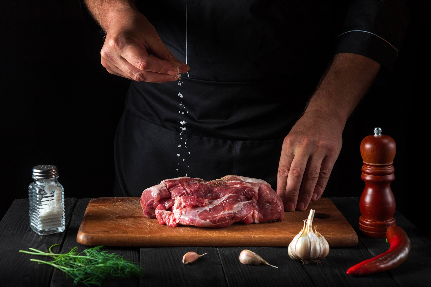 Professional chef sprinkles the meat with salt. Preparing meat b